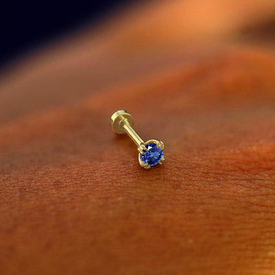 A solid 14k yellow gold Sapphire Flatback Piercing resting on the back of a model's hand