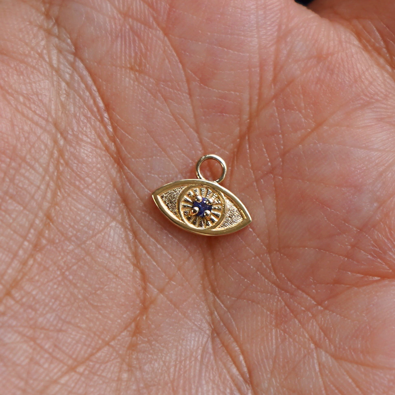 A solid gold blue sapphire Evil Eye Charm for earring resting in a model's palm