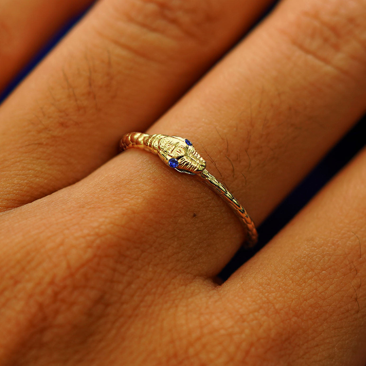 Close up view of a model's hand wearing a yellow gold sapphire Gemstone Ouroboros Snake Ring
