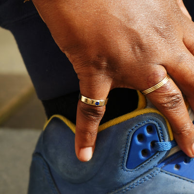 A hand adjusting a shoelace on a sneaker wearing a sapphire Gemstone Industrial Ring and a stack of three Line Rings