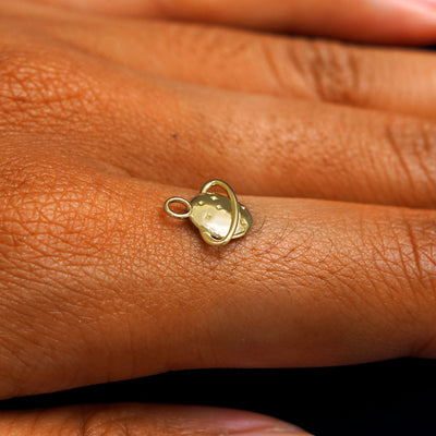 A 14k yellow gold Saturn Charm for chain balancing on the back of a model's finger
