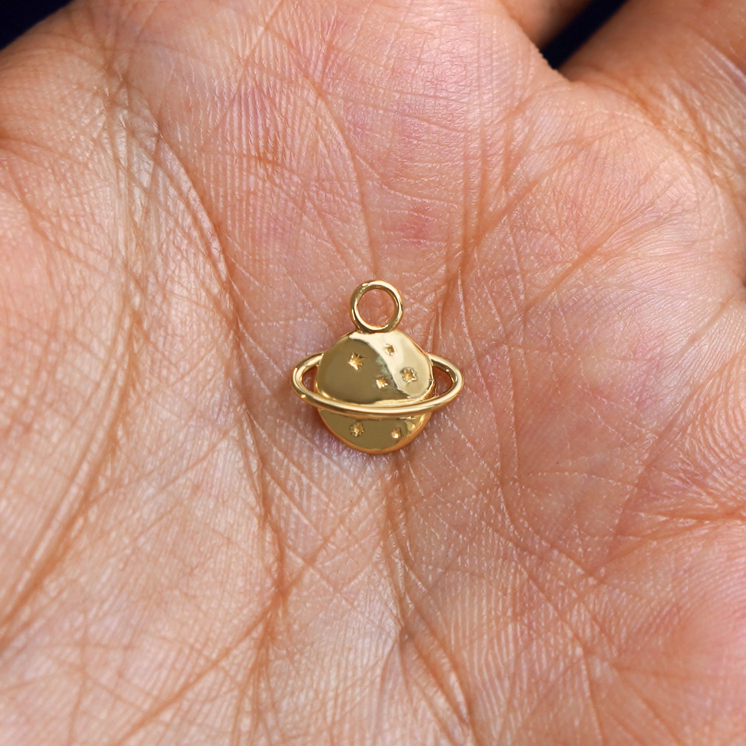 A solid gold Saturn Charm for chain resting in a model's palm