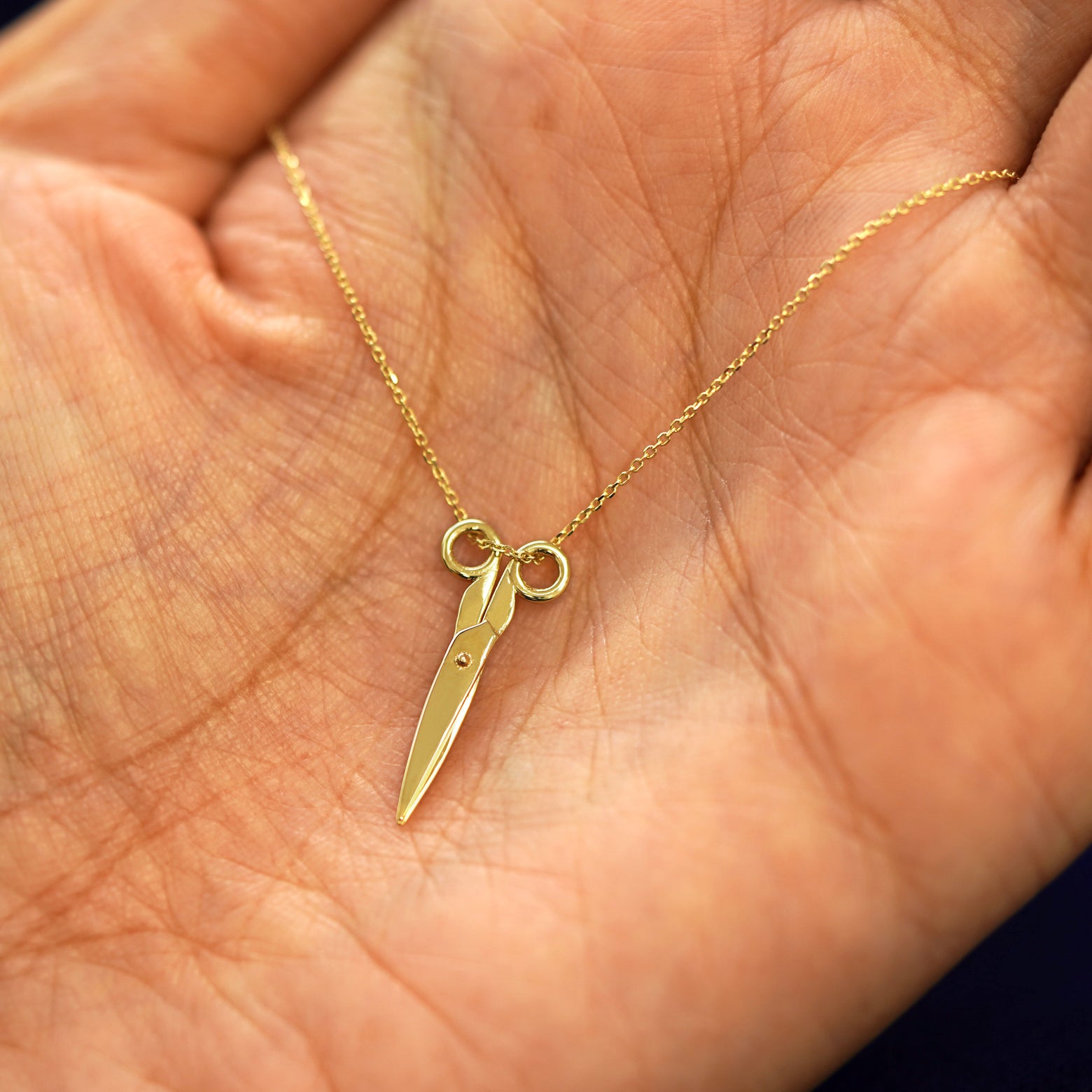 A yellow gold Scissors Necklace draped on a model's palm with the scissors shown closed