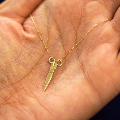 A yellow gold Scissors Necklace draped on a model's palm with the scissors shown closed