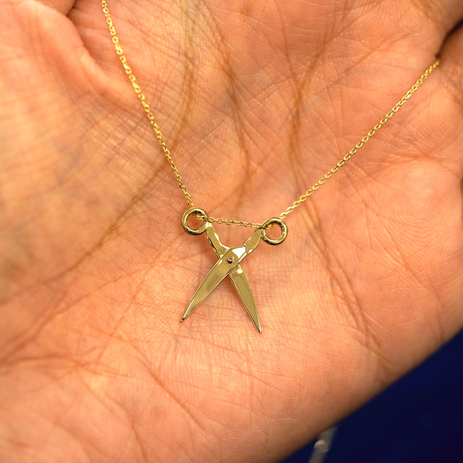 A yellow gold Scissors Necklace draped on a model's palm with the scissors shown open