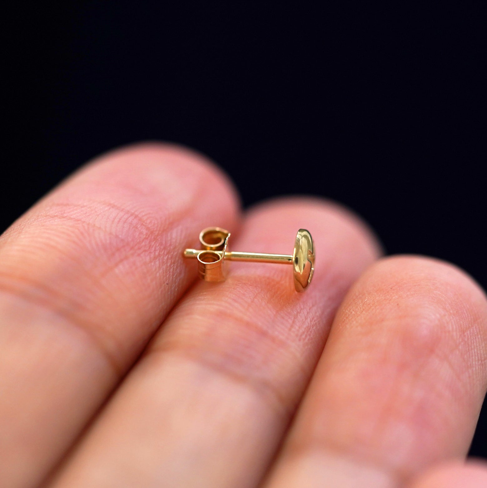 A 14k gold Screw Earring sitting sideways on a model's fingertips to show detail