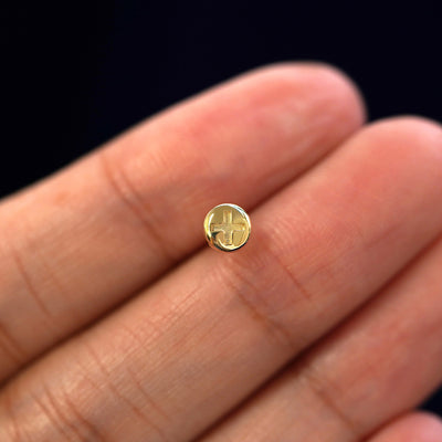 A solid 14k yellow gold Screw Earring in between a model's fingers