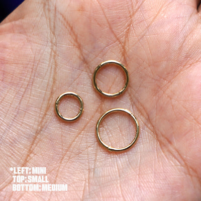 Three versions of the Seamless Huggie Hoop / Piercing shown in options of Mini, Small, and Medium resting in a model's palm