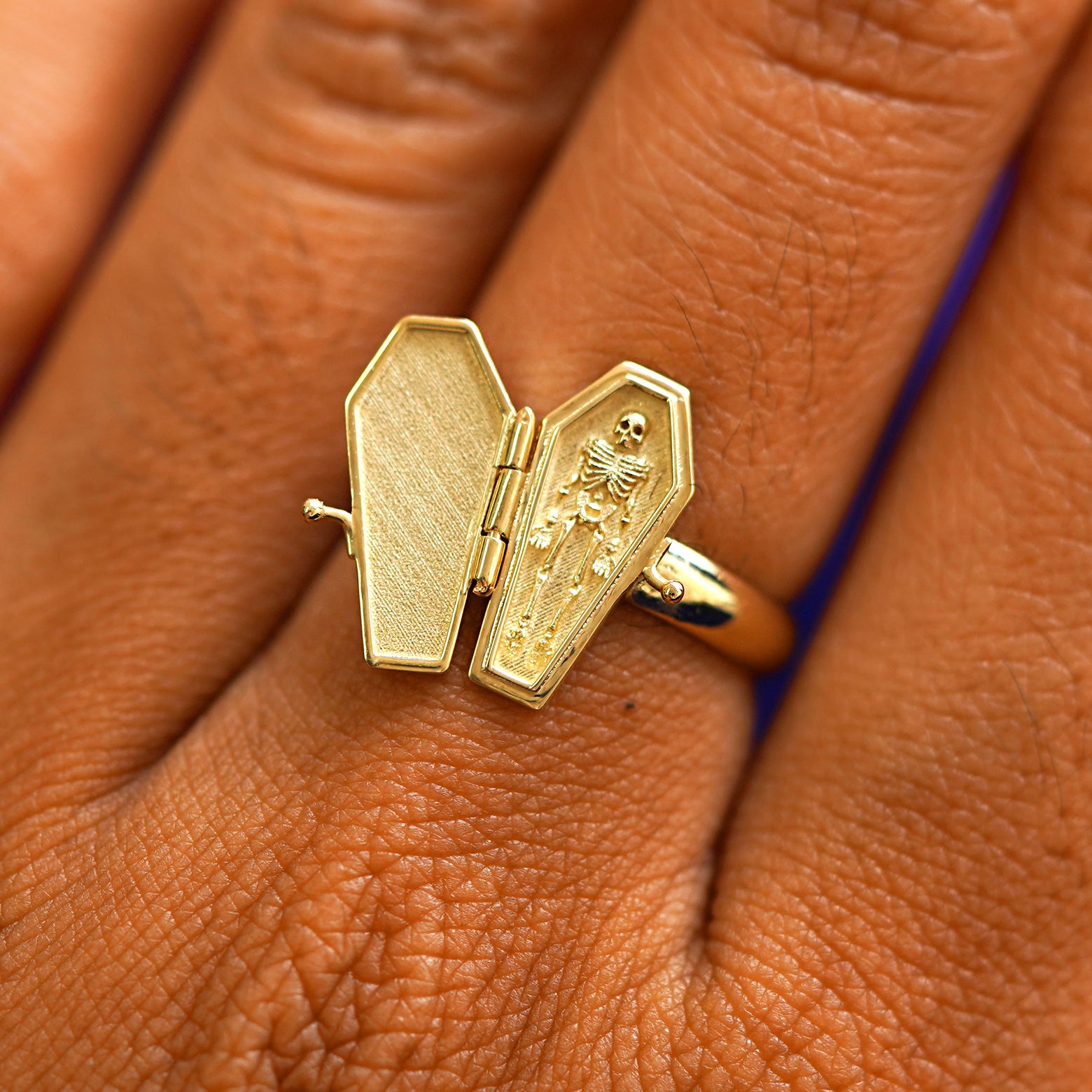 Close up view of a model's hand wearing a yellow gold Coffin Ring in the open position