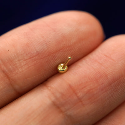 A yellow gold Small Ball Earring laying facedown on a model's fingers to show the underside view