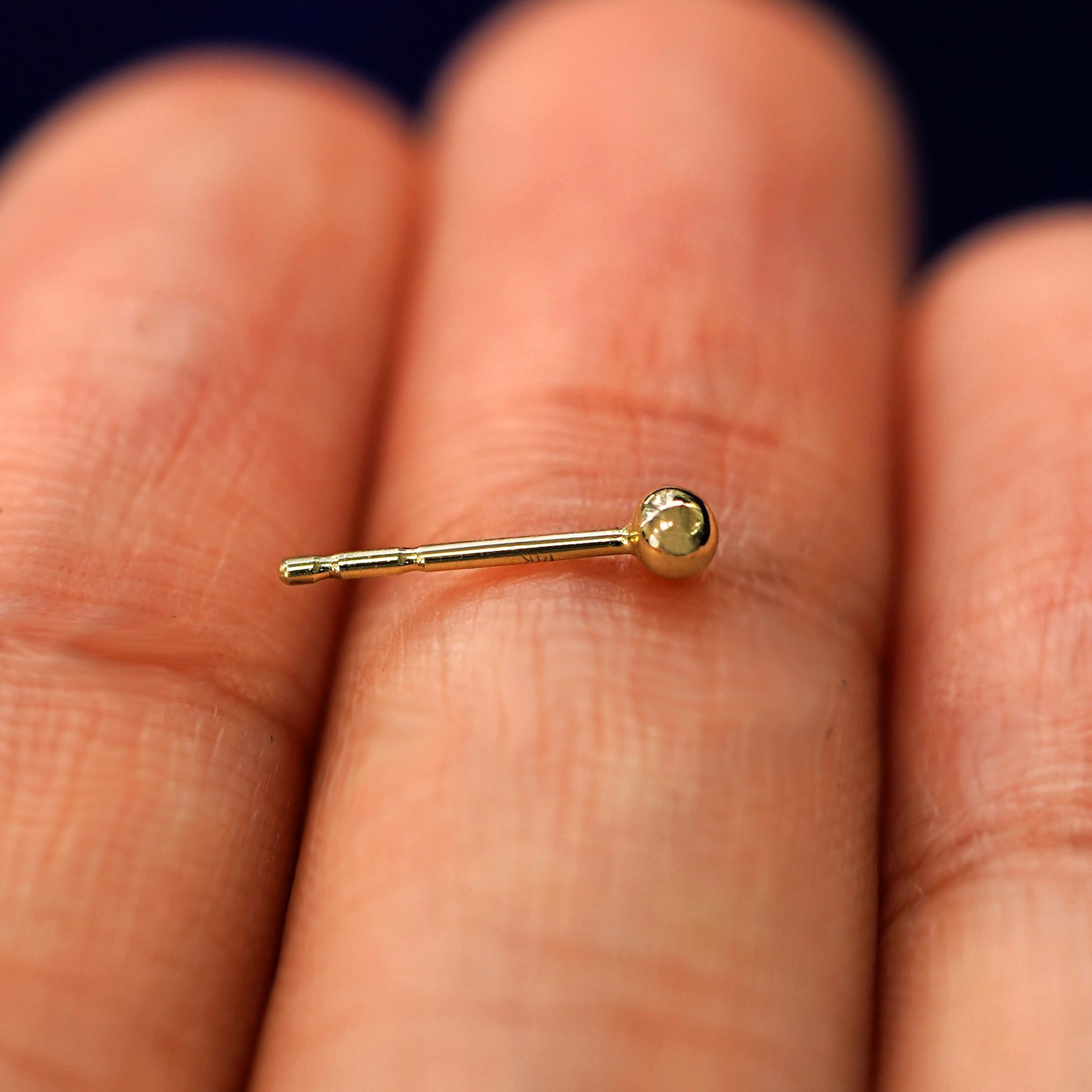 A 14k gold Small Ball Earring sitting sideways on a model's fingertips to show detail