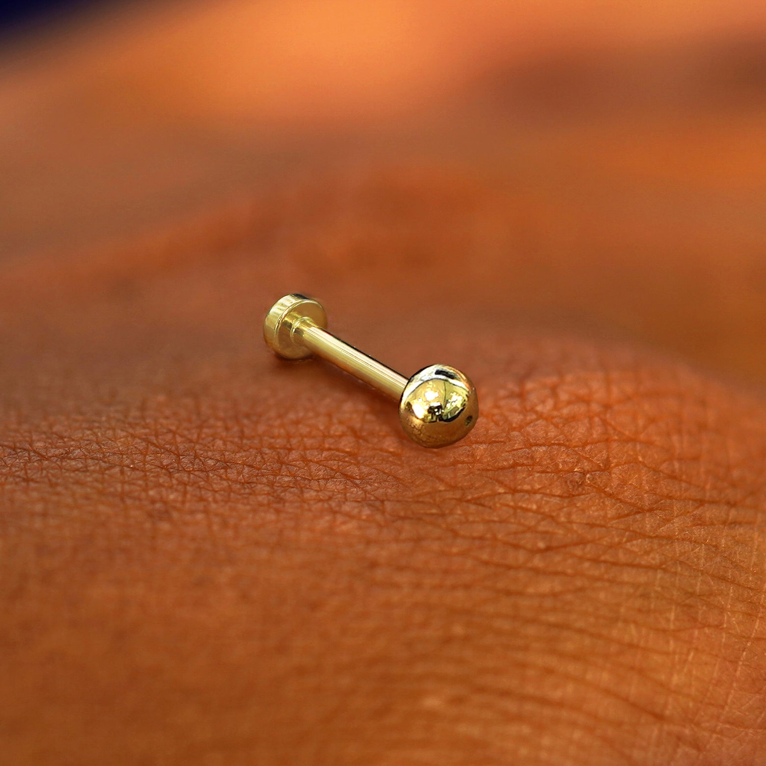 A yellow gold Small Ball Flatback Piercing laying on the back of a model's hand