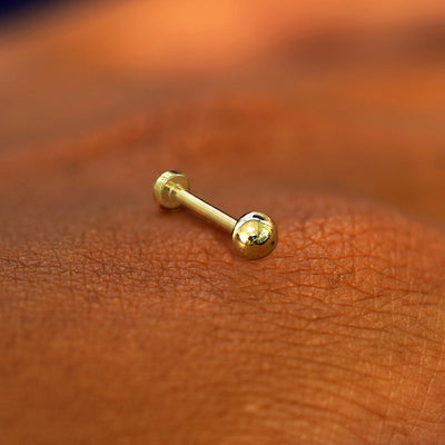 A yellow gold Small Ball Flatback Piercing laying on the back of a model's hand