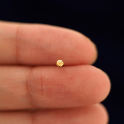 A solid 14k yellow gold Small Ball Earring in between a model's fingers