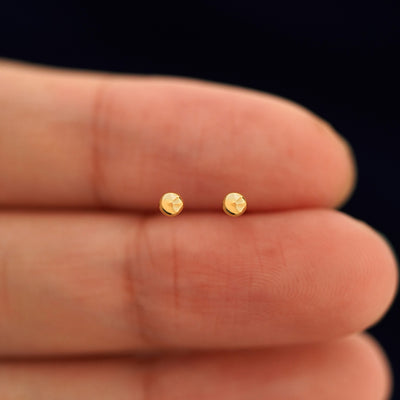 A pair of solid 14k yellow gold Small Ball Earring in between a model's fingers