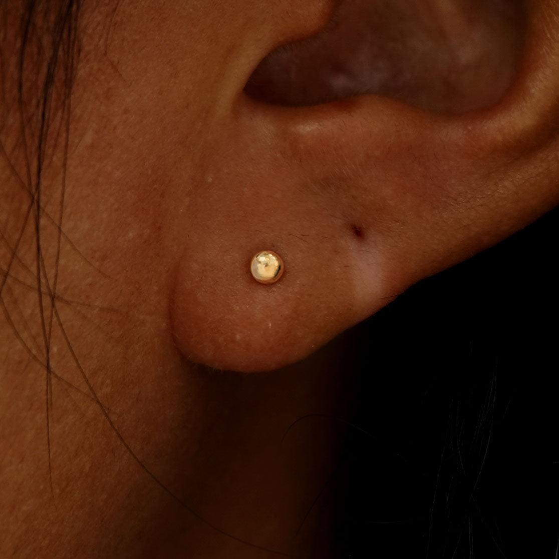 Close up view of a model's ear wearing a yellow gold Small Ball Flatback Piercing