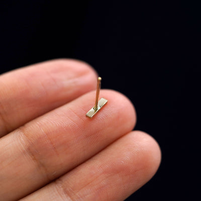 A solid yellow gold Bar Earring laying facedown on a model's finger to show the post and underside of the earring