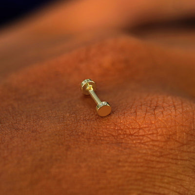 A solid 14k yellow gold Small Circle Flatback Piercing resting on the back of a model's hand