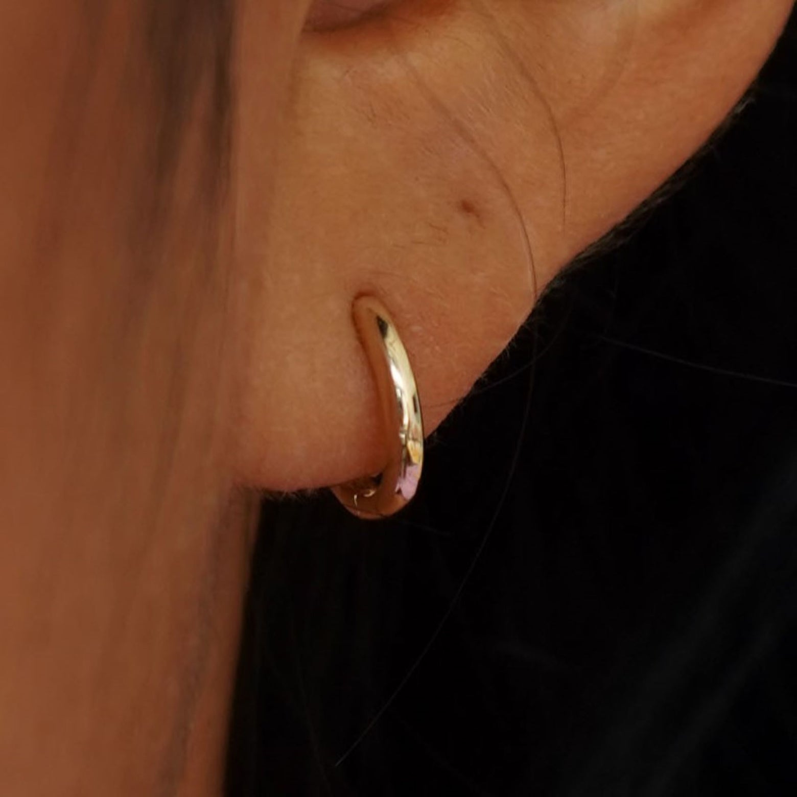 Close up view of a model's ear wearing a yellow gold Small Curvy Huggie Hoop