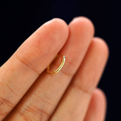 A 14k gold Small Curvy Huggie Hoop Earring held in between a model's fingers to show the hoops thickness