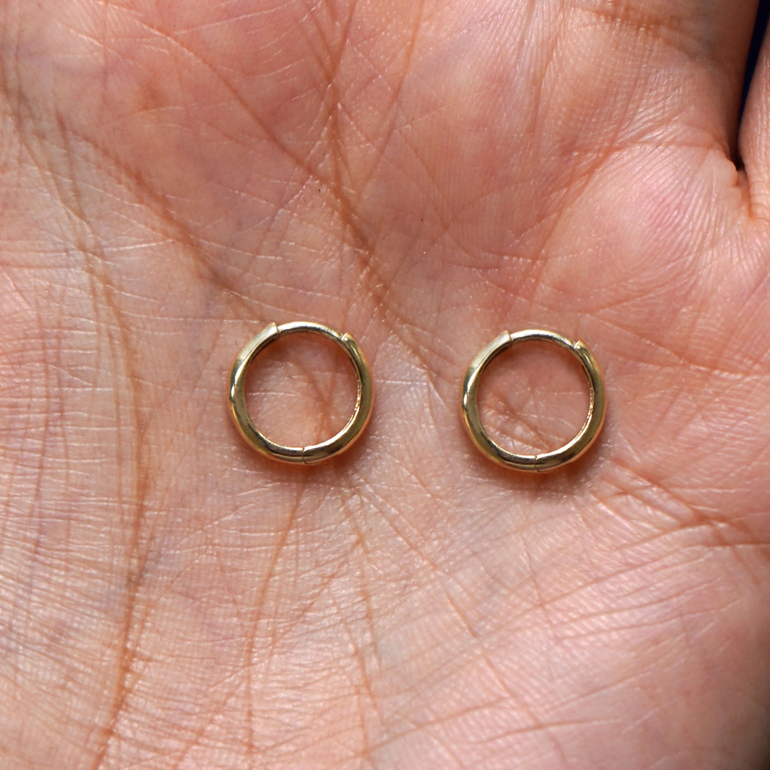 A pair of 14k gold Small Curvy Huggie Hoop Earring sitting in a model's palm
