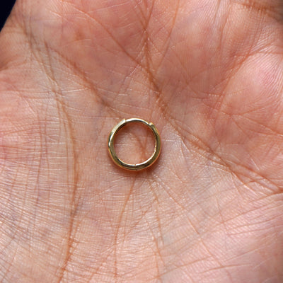 A solid 14k yellow gold Small Curvy Huggie Hoop Earring closed in a model's palm