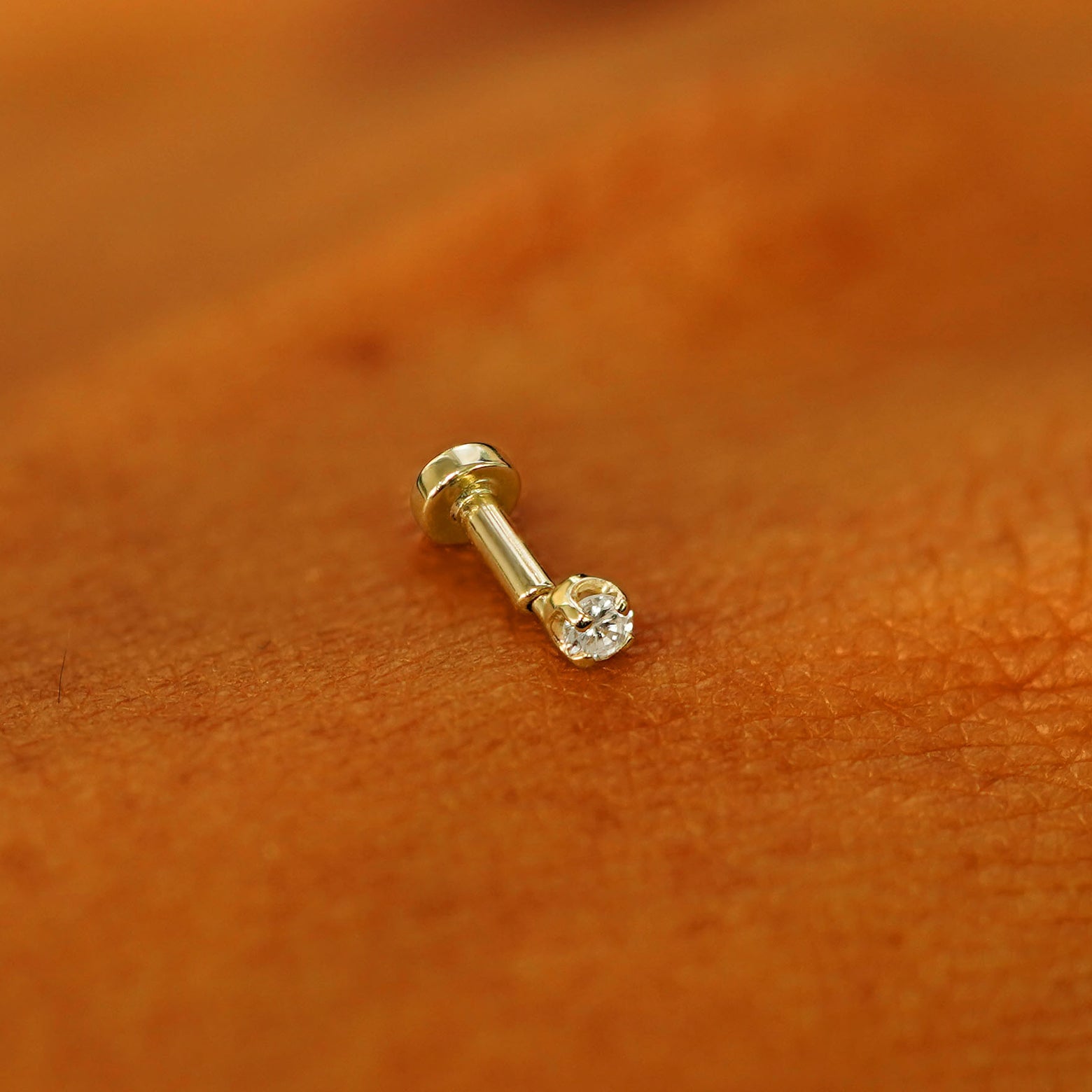 A solid 14k yellow gold 2mm Diamond Flatback Piercing resting on the back of a model's hand