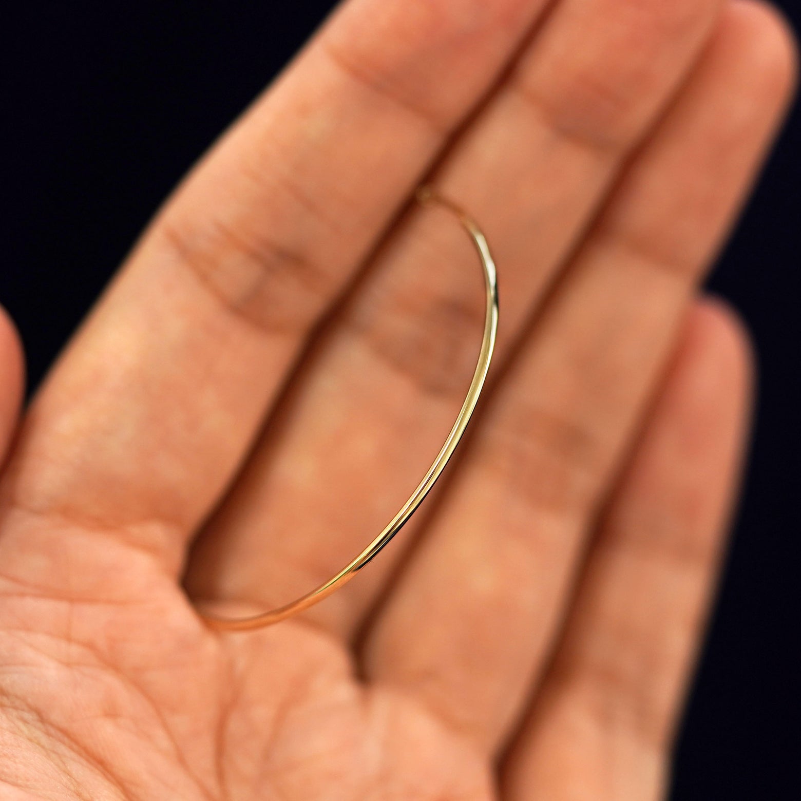 A 14k gold Small Endless Hoop Earring held in between a model's fingers to show the hoops thickness