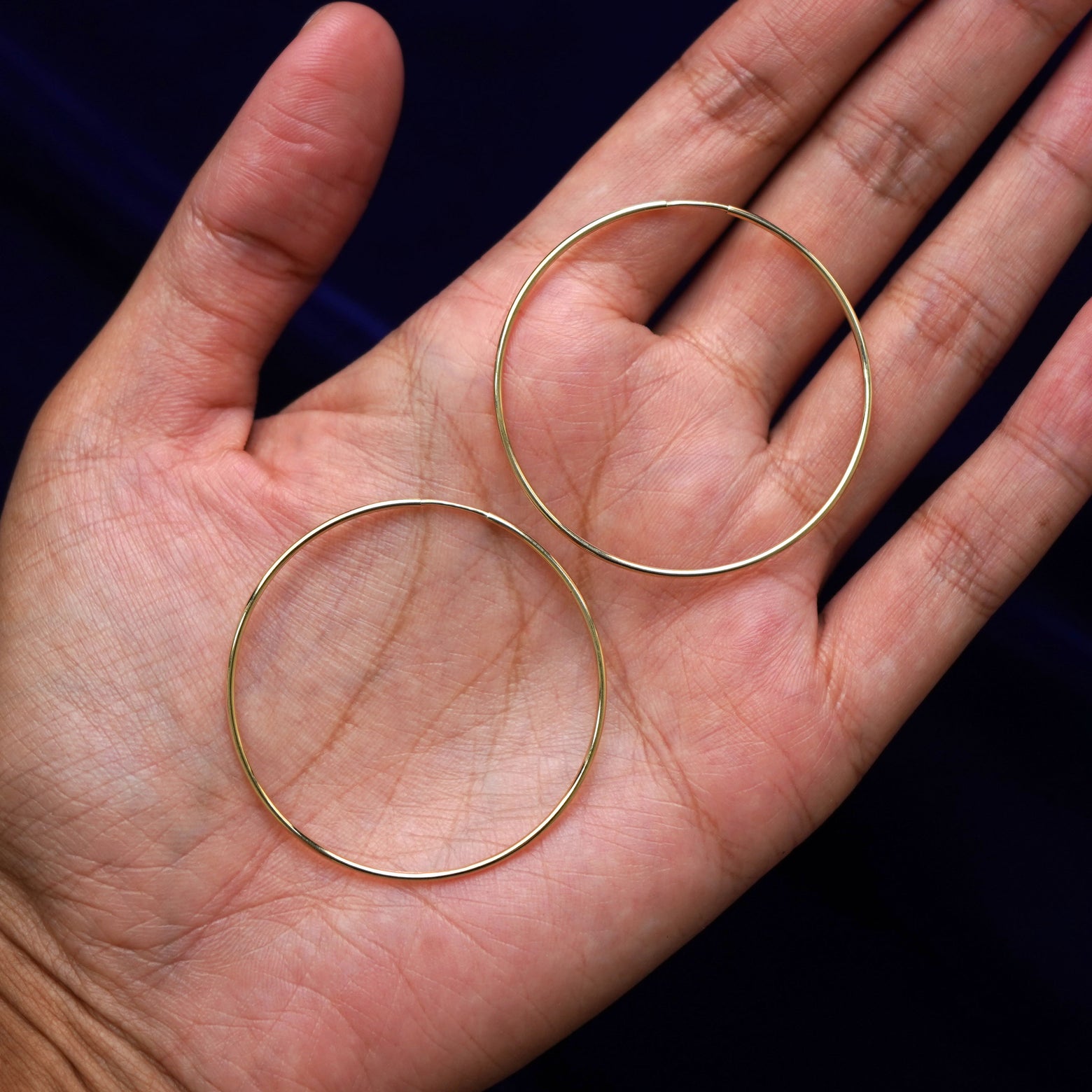 A pair of 14k gold Small Endless Hoop Earring sitting in a model's palm