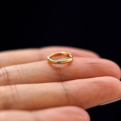 A yellow gold Small Curvy Huggie Hoop Earring laying sideways on a model's fingertips