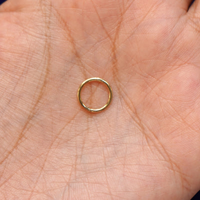 A model holding a closed yellow gold Mini Seamless Huggie Hoop in their palm