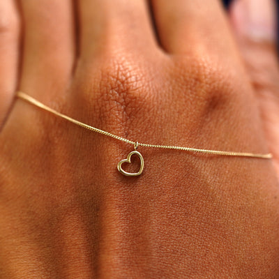 A solid gold Heart Necklace resting on the back of a model's hand