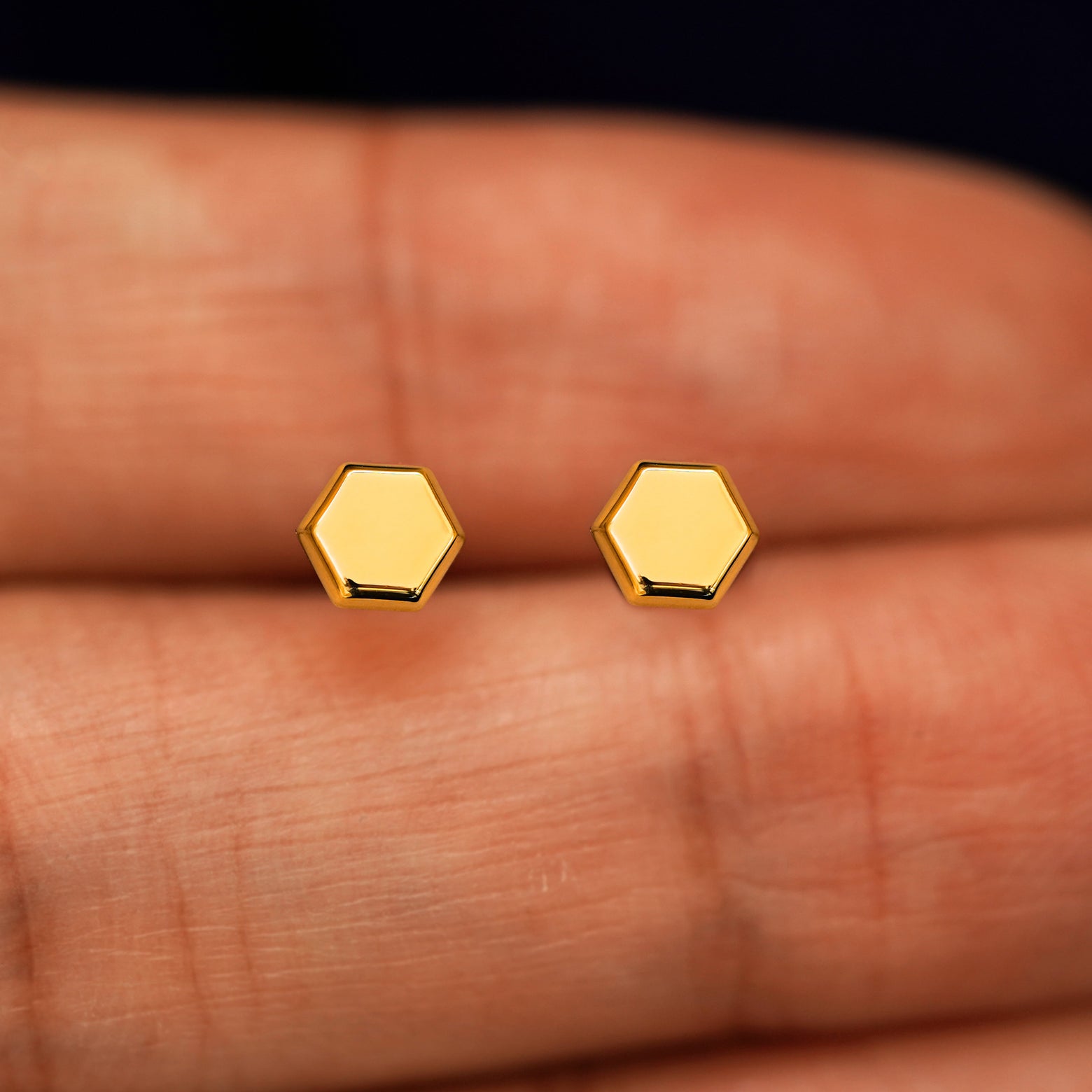 A pair of solid yellow gold Hexagon Earrings in between a model's fingers