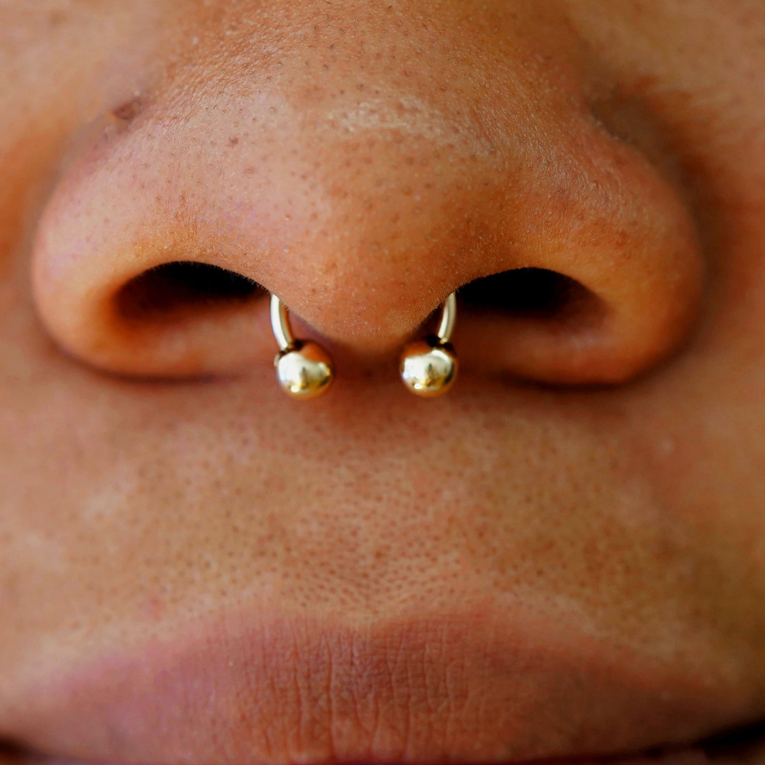 Close up view of a model wearing a yellow gold Small Horseshoe piercing in their septum