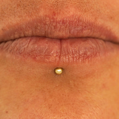 Close up view of a model's lips wearing a 14k yellow gold Small Labret Piercing