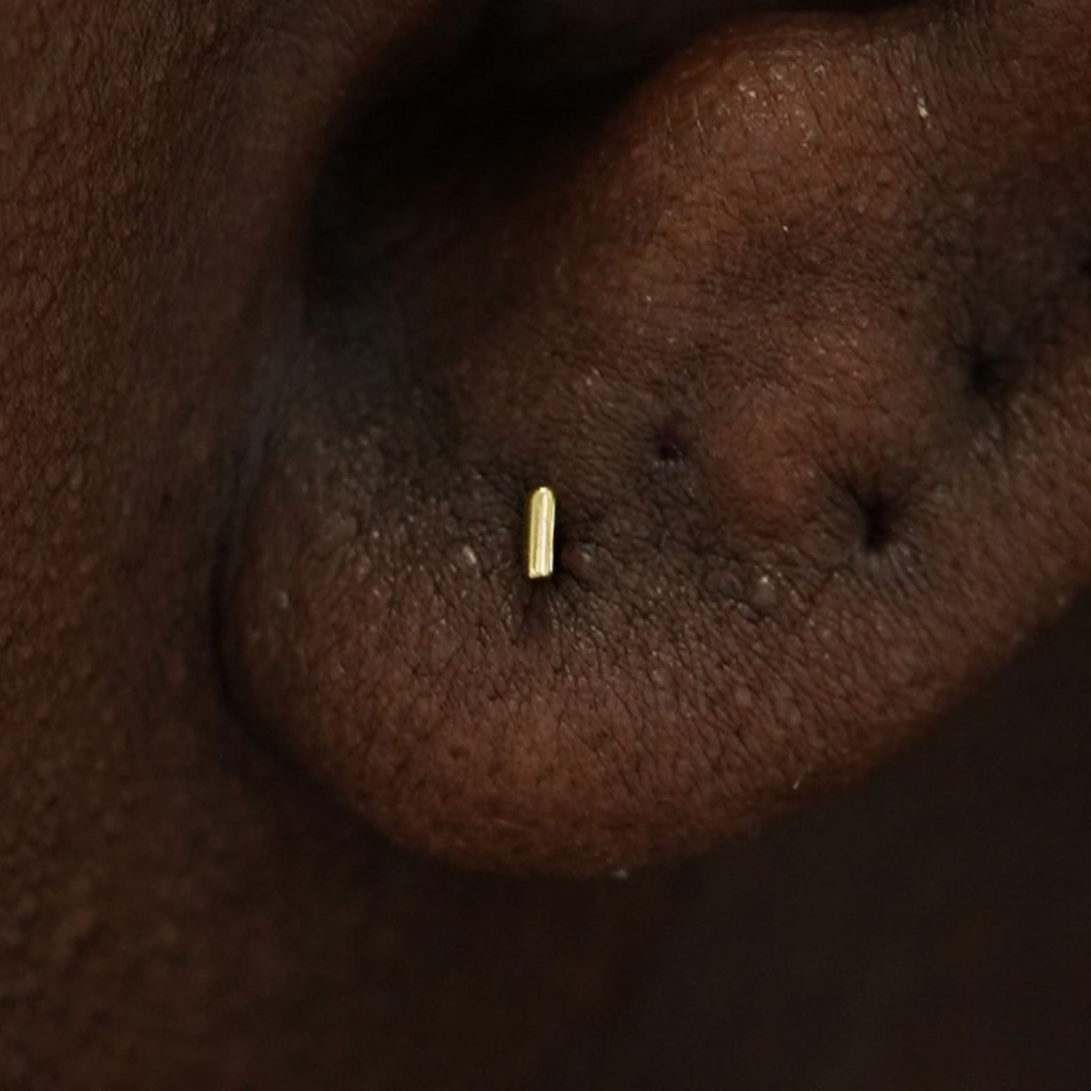 Close up view of a model's ear wearing a 14k gold Small Line Earring