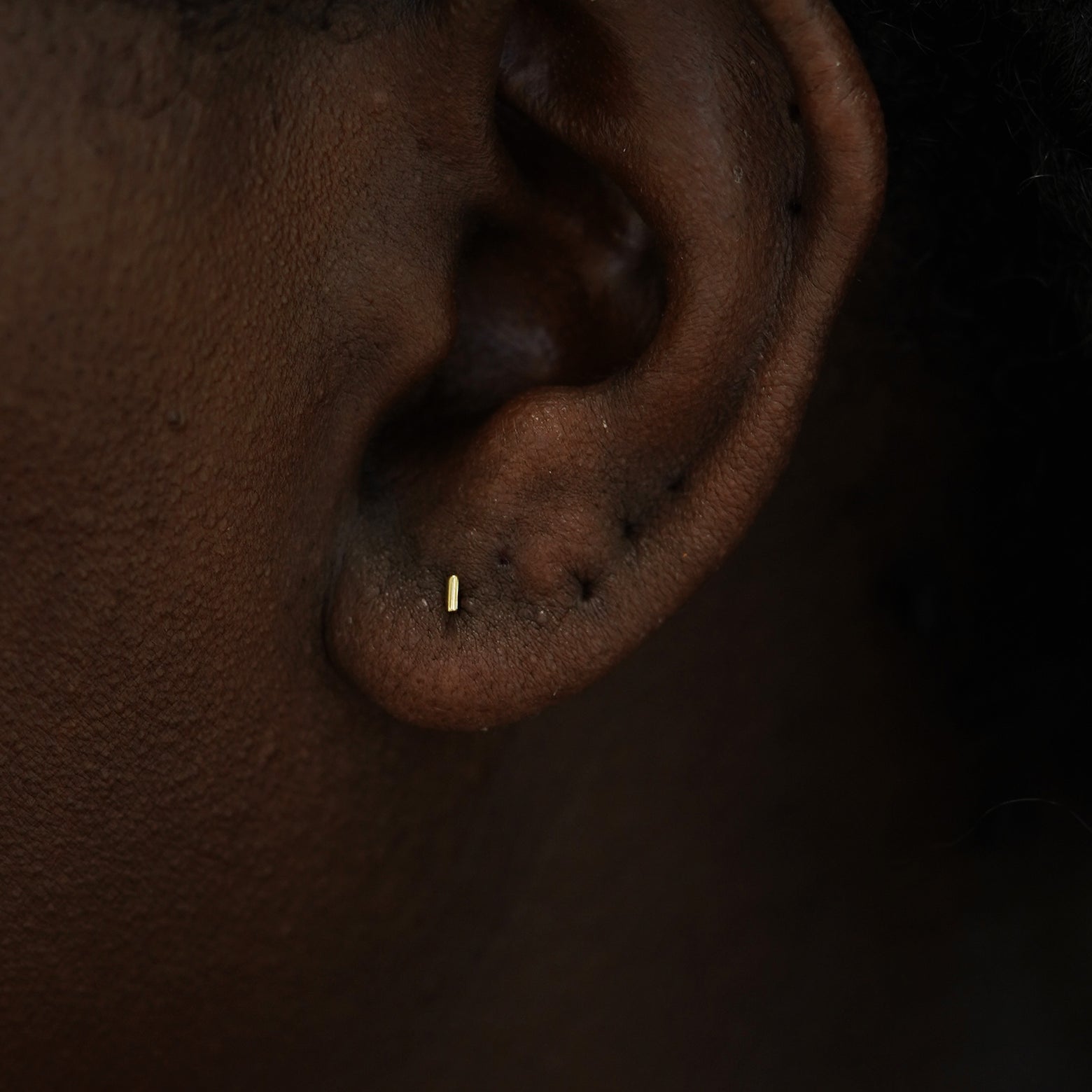 A model's ear wearing a 14k yelllow gold Small Line Earring