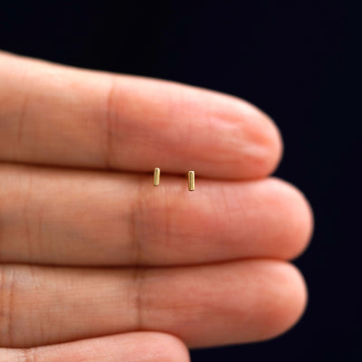 A model's hand holding a pair of recycled 14k gold Small Line Earrings