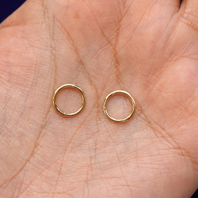 A pair of 14 karat solid gold Small Seamless Huggie Hoops / Piercings in a model's palm