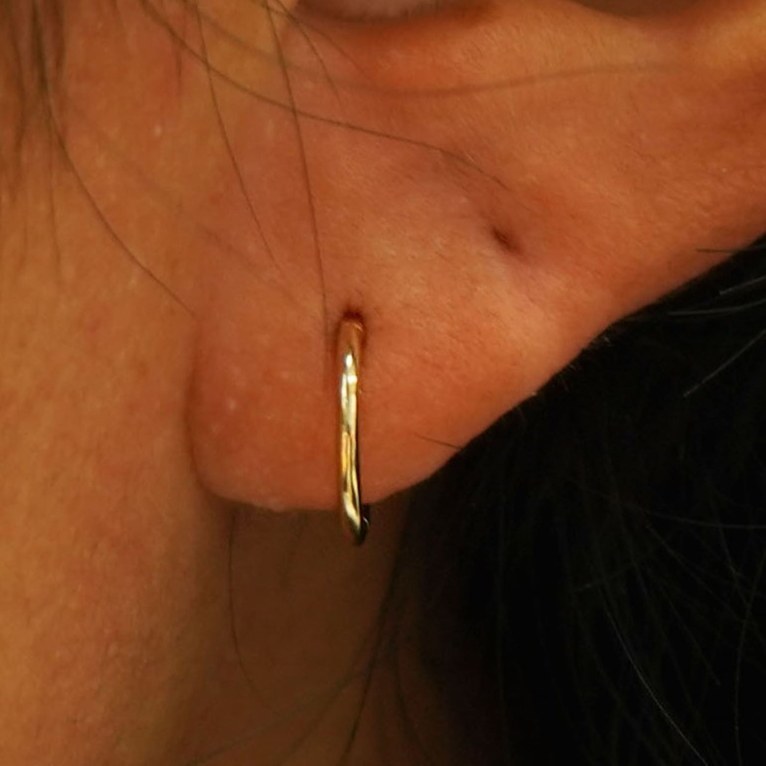 Close up view of a model's ear wearing a yellow gold Small Seamless Huggie Hoop / Piercing
