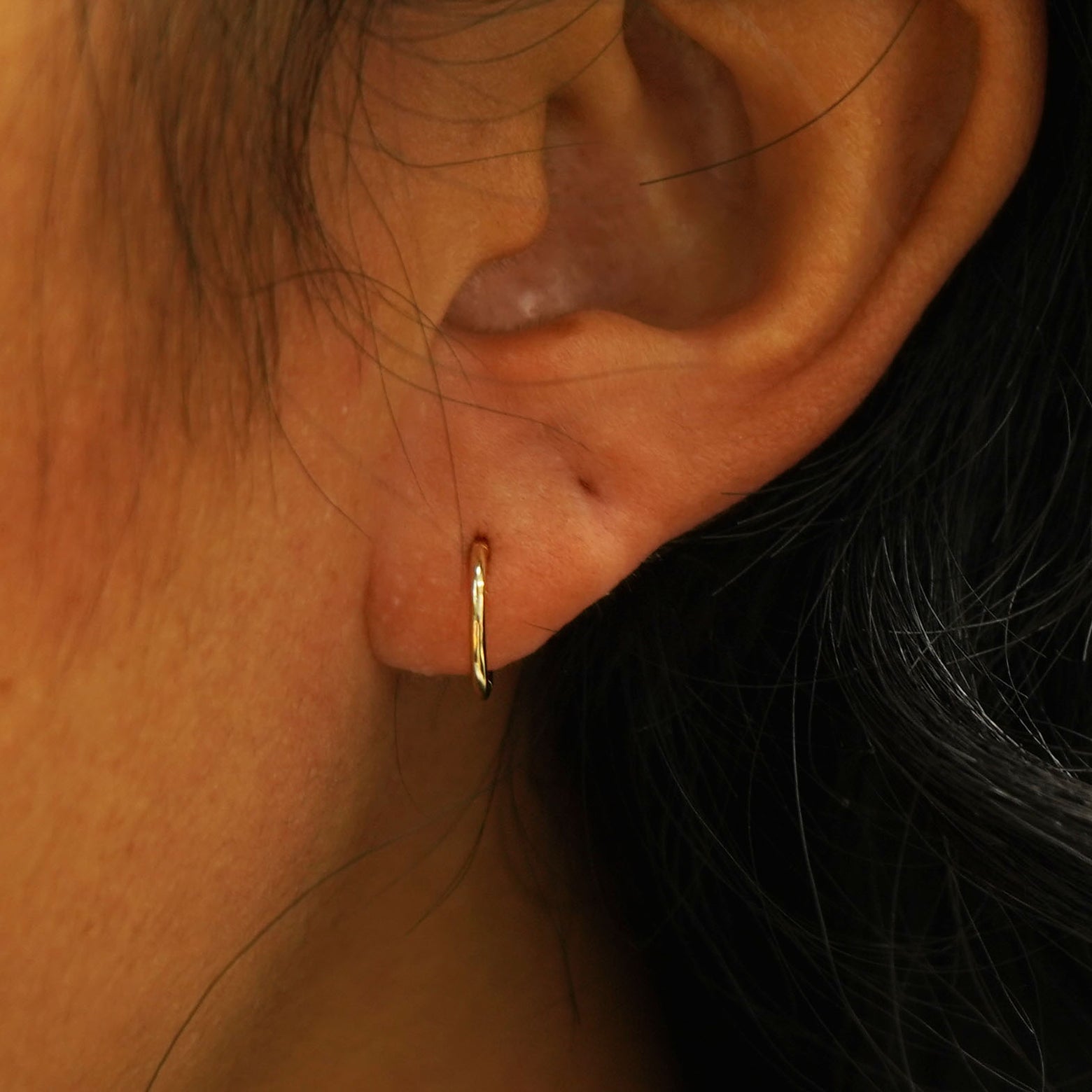A model's ear wearing a 14k gold Small Seamless Huggie Hoop / Piercing