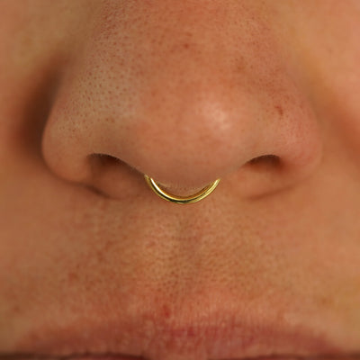 Close up view of a model's nose wearing a 14k yellow gold Small Seamless Huggie Hoop in a septum piercing