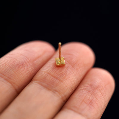 A yellow gold Square Earring laying facedown on a model's fingers to show the underside view