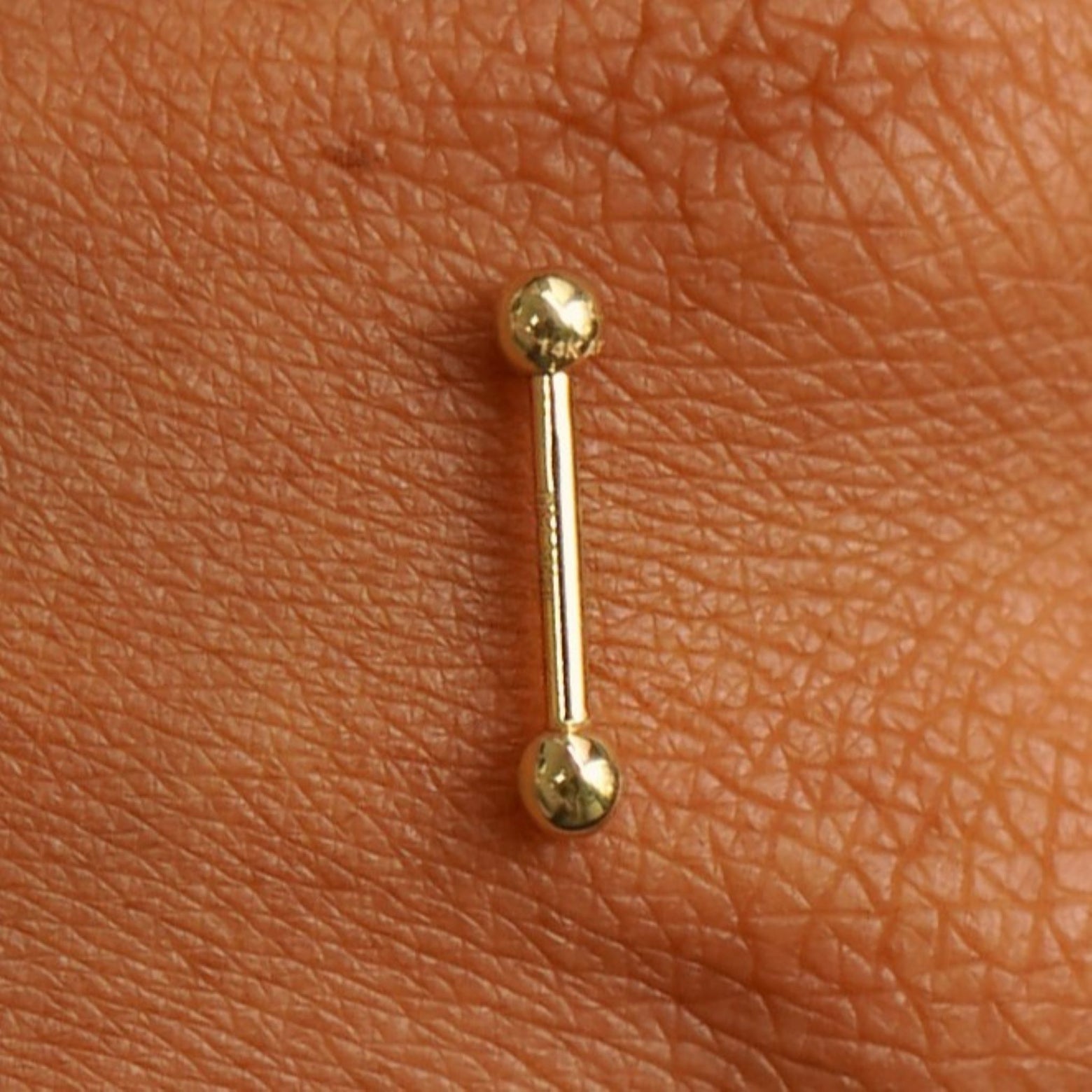 Close up view of a 14 karat gold Small Straight Barbell Piercing resting on the back of a model's hand