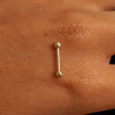 A yellow gold Small Straight Barbell Piercing resting on the back of a model's hand