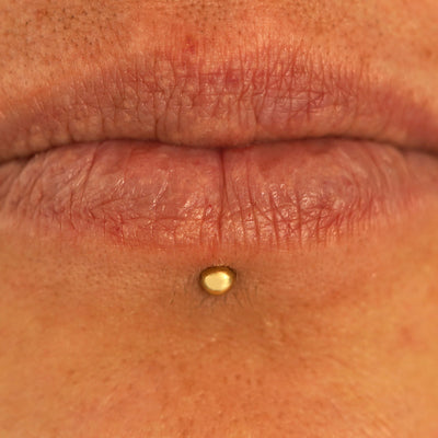 Close up view of a model's lips wearing a 14k yellow gold Small Straight Barbell in a labret piercing