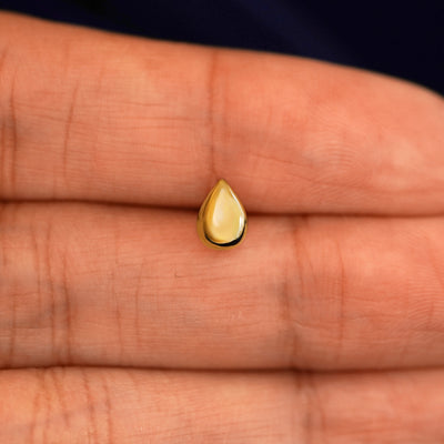 A solid 14k yellow gold Teardrop Earring in between a model's fingers