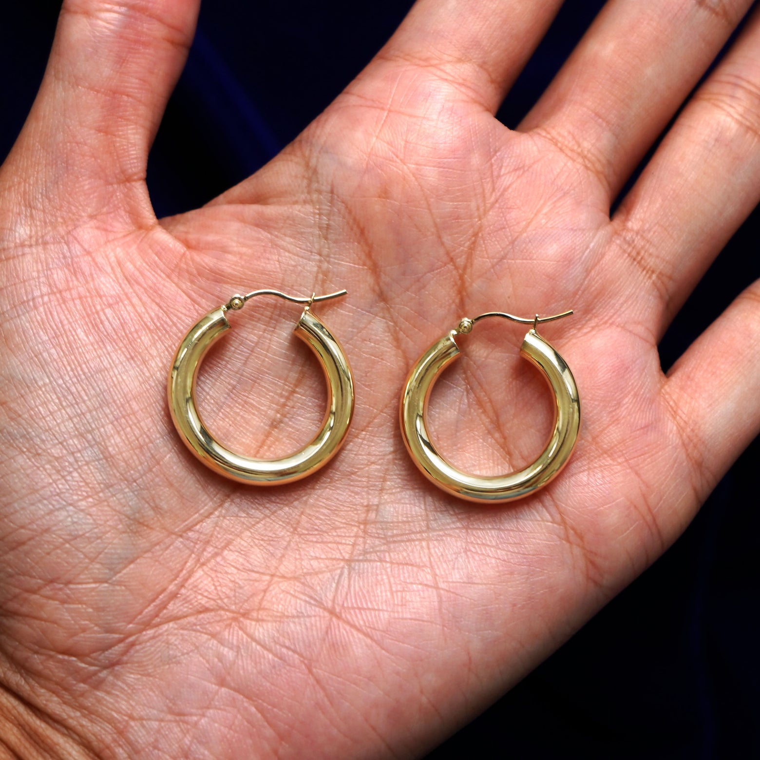 A pair of 14k gold Small Tube Hoop Earring sitting in a model's palm