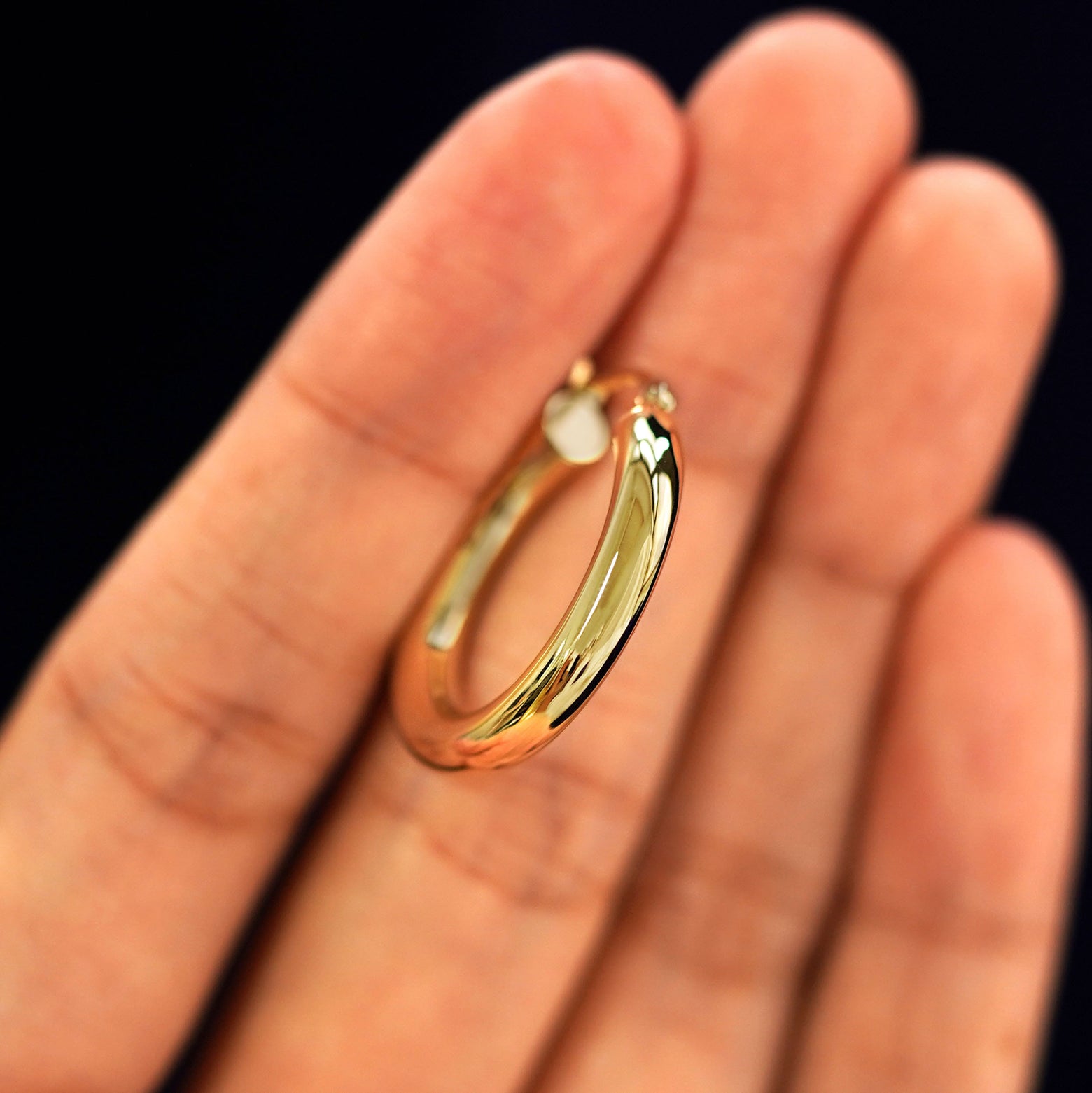 A 14k gold Small Tube Hoop Earring held in between a model's fingers to show the hoops thickness