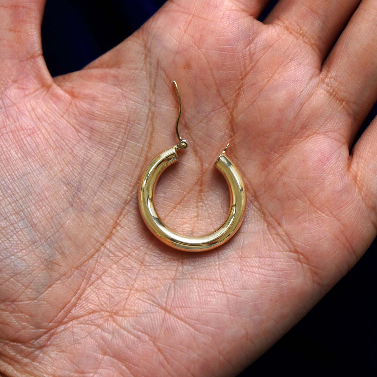 A solid 14k yellow gold Small Tube Hoop Earring open in a model's palm to show the hinge